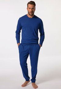 Blusa azul de manga larga con escote en V y bolsillo, combinada con pantalones elásticos azules a juego. Tejido suave, corte relajado, sin patrones ni acentos.