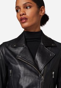 Schwarze Leder-Motorradjacke mit asymmetrischem Reißverschluss, breiten Revers und silbernen Hardware-Details. Glatte Textur mit taillierter Passform.