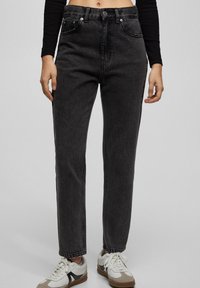 Högmidjade svarta jeans i denim med rak ben, fem fickor, bälteshällor och subtil slitning. I kombination med vita och beige sneakers.