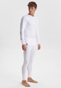 Hvit termisk langermet topp med rund hals og tre-knapps stolpe, kombinert med matchende tettsittende lange bukser. Myk tekstur og tettsittende passform.