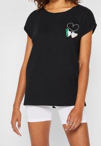 Svart bomull T-shirt med uppvikt korta ärmar, med broderade hjärtan och irländska flaggdetaljer på framsidan. Avslappnad design.