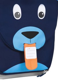 Dunkelblauer Rucksack mit einem Bärenkopf-Design, das eine hellblaue Nase und einen orangefarbenen Namensschildhalter an der Zunge aufweist.