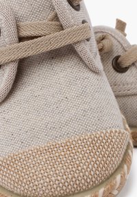 Sneaker in tela beige con una toma superiore texturizzata, occhielli rotondi marroni, lacci beige e un accento in corda di juta lungo la suola.