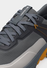 Κοντινή λήψη γκρι αθλητικού παπουτσιού Columbia με πλεκτό ύφασμα, χοντρές κορδόνια και κίτρινη λεπτομέρεια στη σόλα και στη θηλιά του κορδονιού.