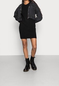 Abito nero lavorato a maglia, giacca in denim nera cropped con cuciture visibili e stivali combat neri con lacci e suola chunky.