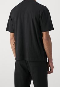 Schwarzes Baumwoll-T-Shirt mit kurzen Ärmeln und Rundhalsausschnitt, gerade geschnitten und mit glatter Textur. Rückansicht, ohne Grafik.