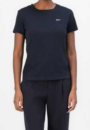 Persoon die een marineblauw T-shirt met korte mouwen en bijpassende broek draagt, staand tegen een effen witte achtergrond.