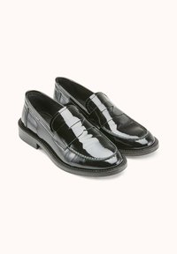 Mocassins en cuir verni noir avec une finition lisse, présentant un bout cousu et un petit talon carré. Design minimaliste sans accents proéminents.