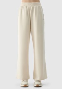 Beige weite Sweathosen mit einem elastischen Bund, seitlichen Taschen und einer glatten Textur. Kombiniert mit hellen Sneakers für den Kontrast.