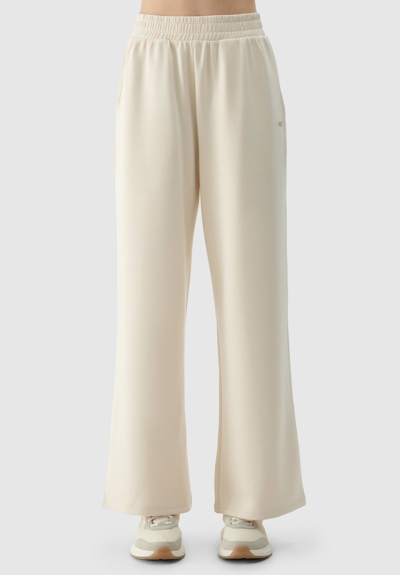 Beige weite Sweathosen mit einem elastischen Bund, seitlichen Taschen und einer glatten Textur. Kombiniert mit hellen Sneakers für den Kontrast.