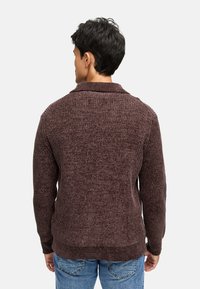Brun struktureret striktrøje med krave, lange ærmer og ribbede detaljer, parret med blå jeans. Bagfra.