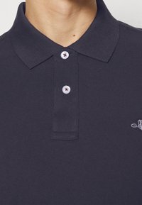 Polo navy en tissu texturé, avec un col, une patte de boutonnage à deux boutons et un petit logo brodé sur la poitrine.