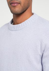 Pulover lavandă deschisă cu un design tricotat texturat și un guler rotund cu nervuri, realizat dintr-un material moale și ușor elastic.