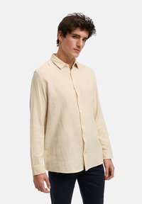 Langärmliges Hemd in hellbeige, aus strukturiertem Stoff mit lockerer Passform, klassischem Kragen und durchgehender Knopfleiste.