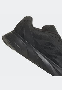 Baskets de sport noires avec tige en mesh, semelle épaisse et rembourrée étiquetée « Lightmotion », et texte sur le panneau latéral « Duramos » sur le support de talon.