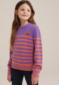 Pulover s purple in oranžnimi črtami, mehkega in puhastega videza; na njenem prsnem delu je majhna oranžna vezenina oblike srca, rokavi pa so z ribastim zaključkom.