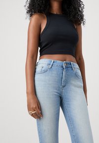 Black ribbed crop top with wide straps paired with light blue high-waisted jeans. Fabric is smooth with slight distressing near pockets.