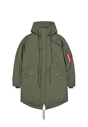 Olivovo zelená parka s kapucňou, predným zipsom, šnúrkami, klopovými vreckami a červeným označením "Remove Before Flight" na vrecku ľavého rukáva.