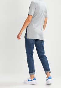 Grå kortärmad skjorta, blå denimjeans med uppvikta fållar, och vita sneakers med blå detaljer, vy från baksidan.