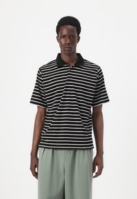 Striped polo shirt in black and white, featuring a black collar and short sleeves. Fabric has a textured appearance.