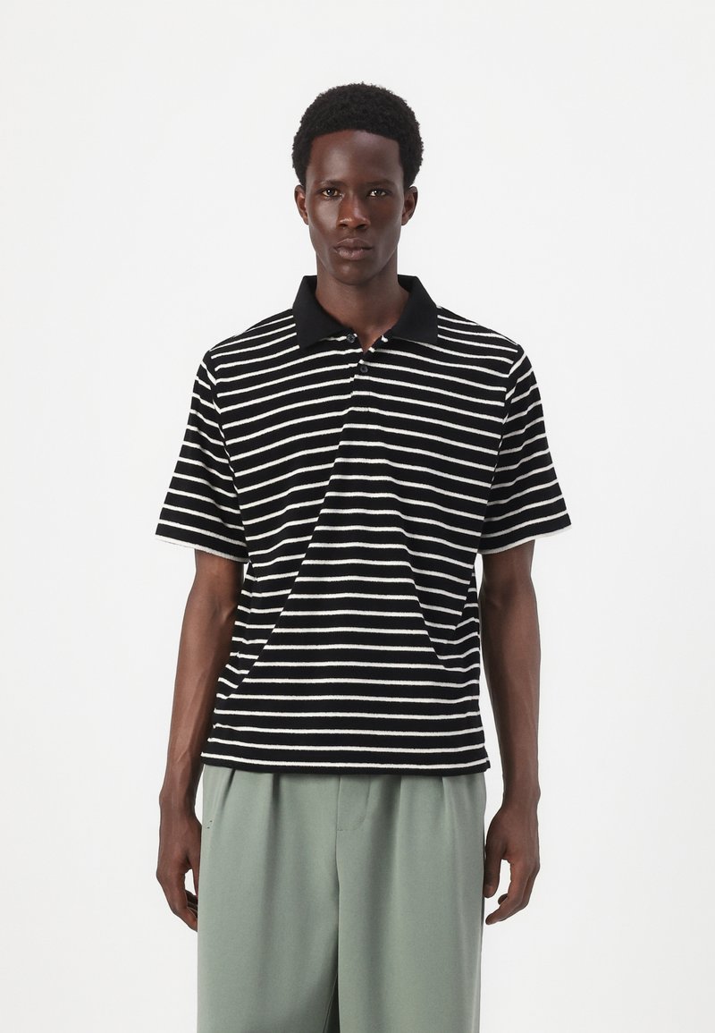 Striped polo shirt in black and white, featuring a black collar and short sleeves. Fabric has a textured appearance.