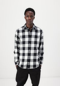 Zwart-witte geblokte langemouwenshirt met een button-down kraag en een licht gestructureerde stof. Een gebogen zoom maakt het ontwerp compleet.