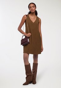 Abito a rilevo marrone senza maniche con scollatura a V, dalla texture liscia. Abbinato a stivali marroni in suede fino al ginocchio e a una piccola borsa bordeaux con catena dorata.