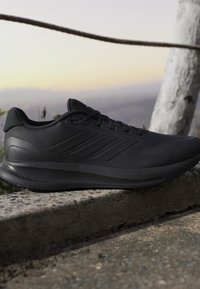 Pantof negru sportiv pentru alergare cu partea superioară texturată și design cu șireturi, odihnindu-se pe un prag de beton în aer liber la apus.