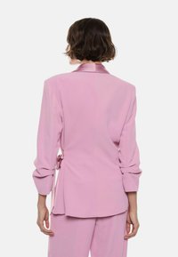 Rosa skræddersyet blazer med satinkrave og pufærmer, med en bagbåndslukning og glat tekstureret stof.