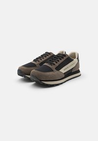 Brune og svarte sneakers med overdel i semsket skinn og tekstil, svarte snører, beige detaljer, gummisåler og preget logo på siden.