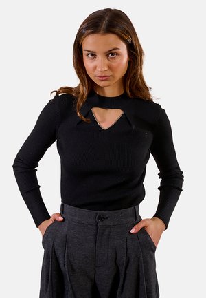 Top lungo a maniche ribbed nera con scollatura rotonda e dettaglio a taglio. Il modello lo abbina a pantaloni grigi a vita alta.