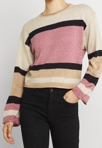 Maglione lavorato a maglia con strisce orizzontali rosa, beige, nere e bianche. Presenta maniche a campana larghe e un colletto rotondo. Tessuto strutturato.