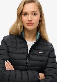 Zwart donzen jack met een hoge kraag, horizontale doorgestikte structuur en een teal voering. Ritssluiting met merklogo op de linkerborst.