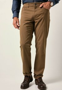 Hnědé bavlněné kalhoty se slim fit, zipovým zapínáním a předními kapsami. V kombinaci s hnědými botami a modrou košilí s dlouhým rukávem.