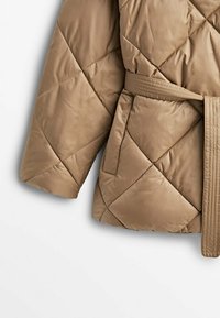 Veste matelassée marron clair avec des surpiqûres diagonales, une ceinture assortie et une poche latérale rectangulaire à l'avant.