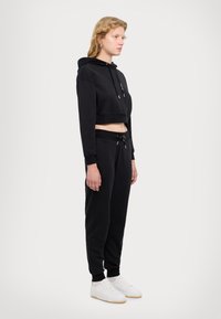 Cropped hoodie nera con coulisse e maniche lunghe; abbinata a pantaloni tuta neri con vita elastica e polsini alla caviglia. Sneakers bianche.