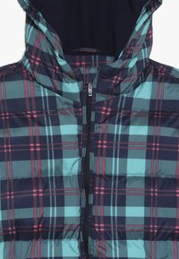 Veste matelassée en doudoune avec un motif à carreaux bleu marine, turquoise et rose, dotée d'une fermeture éclair frontale et d'une capuche. Texture lisse avec des sections rembourrées.