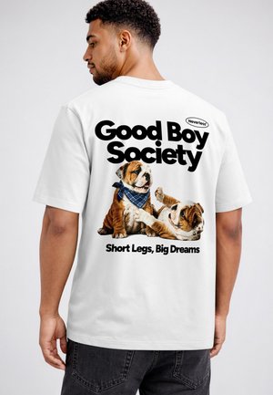 Mann trägt ein weißes T-Shirt mit zwei verspielten Bulldoggen und dem Text "Good Boy Society" und "Short Legs, Big Dreams" auf dem Rücken.