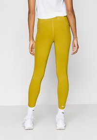 Κίτρινο κολάν με λείο υφή και εφαρμοστή σχεδίαση, με φερμουάρ στην πίσω τσέπη και μικρό λευκό λογότυπο της Nike κοντά στον αστράγαλο.