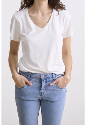 Weißes Baumwoll-V-Ausschnitt-T-Shirt kombiniert mit hellblauen Jeans aus Denim mit Knopfverschluss und doppelten Seitentaschen. Natürliche Stoffstruktur sichtbar.