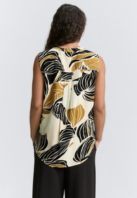 Canotta senza maniche con un motivo floreale in nero e oro su uno sfondo crema, con un orlo arrotondato e dettaglio di pieghe sul retro.