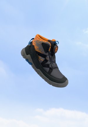 Chaussure de randonnée grise et orange avec des sangles noires et une semelle texturée, flottant sur un fond de ciel bleu clair.