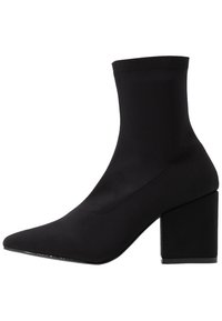 Bottine noire en tissu extensible avec bout pointu, talon bloc et design sans couture. Texture lisse avec des détails de coutures subtiles.