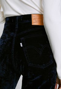 Tmavě modré sametové džíny s koženou nášivkou Levi's, se klasickým pětiokým designem a jemným prošíváním.