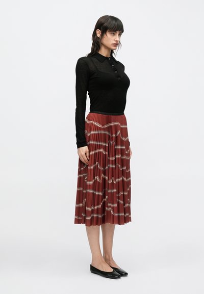 Mustast pikkade varrukatega poloülikond, millel on nööbid, koos plekilise, rooste-punase seelikuga, millel on geomeetriline muster. Komplekti kuuluvad mustad baleriinikingad.