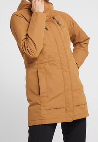 Brązowa ocieplana parka z wysokim kołnierzem, regulowanymi sznurkami, bocznymi kieszeniami i gładką teksturą. Średniej długości konstrukcja zapewniająca ciepło.