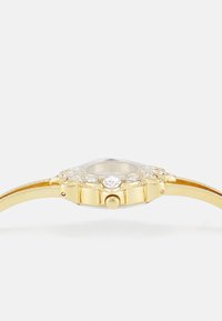 Gold-tone wristwatch with a round case, clear crystal face, and embellished with multiple small gemstones along the bezel for detailing.