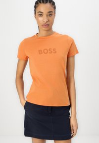 Orange cotton t-shirt with crew neckline, featuring the word "BOSS" printed in darker orange across the front. Short sleeves, fitted design.