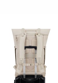 Beige hátizsák ergonómikus pántokkal, hálós hátsó panellel és két alumínium fogantyúval; tetején fedél és cipzáras oldalzseb található.