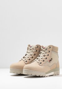 Stivali da trekking beige con una combinazione di materiali lisci e testurizzati, design con lacci, suole in gomma robuste e accenti del logo Fila.